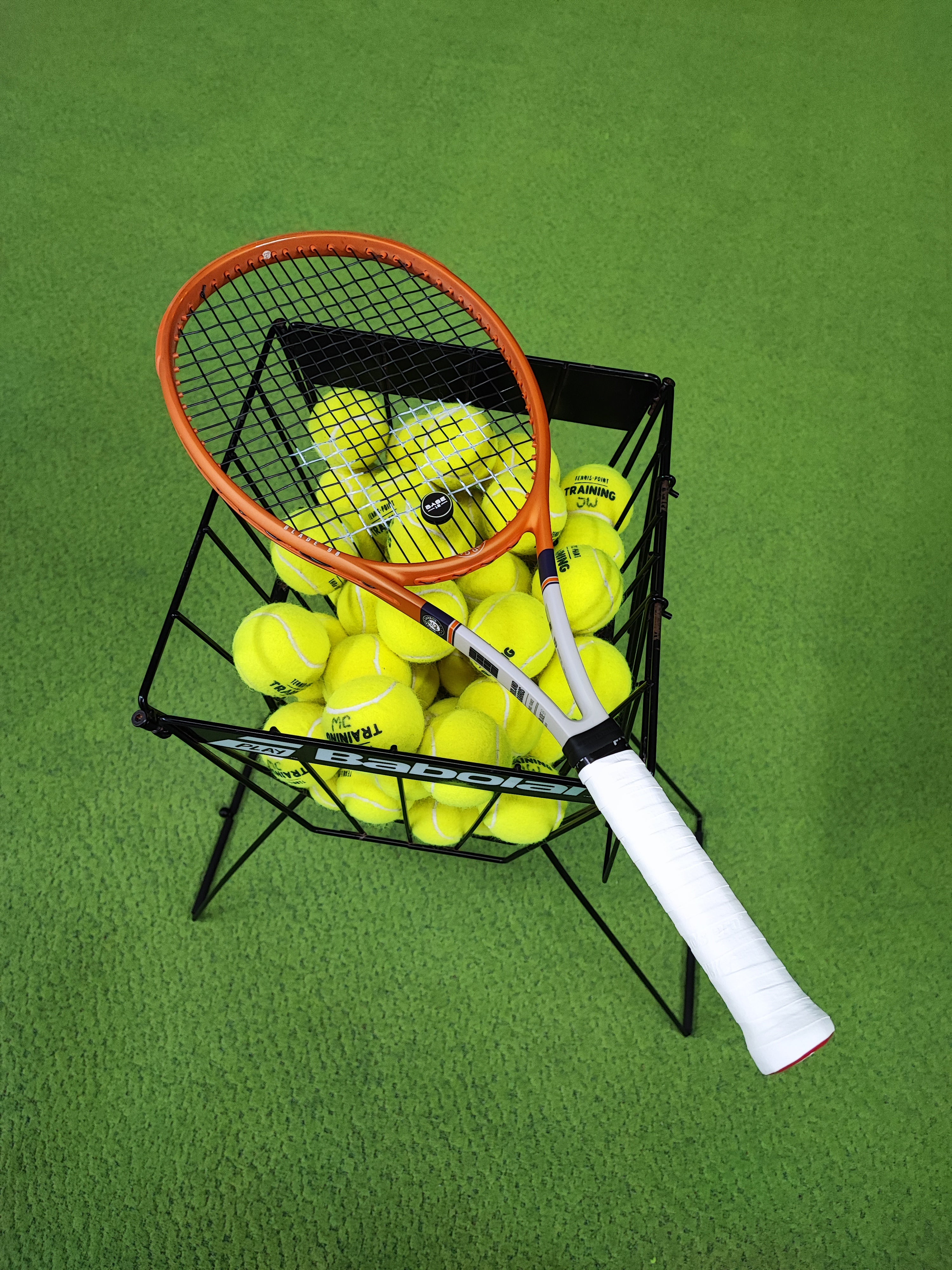Tennisschläger liegt auf einem Ballkorb mit Tennisbällen während des Trainings