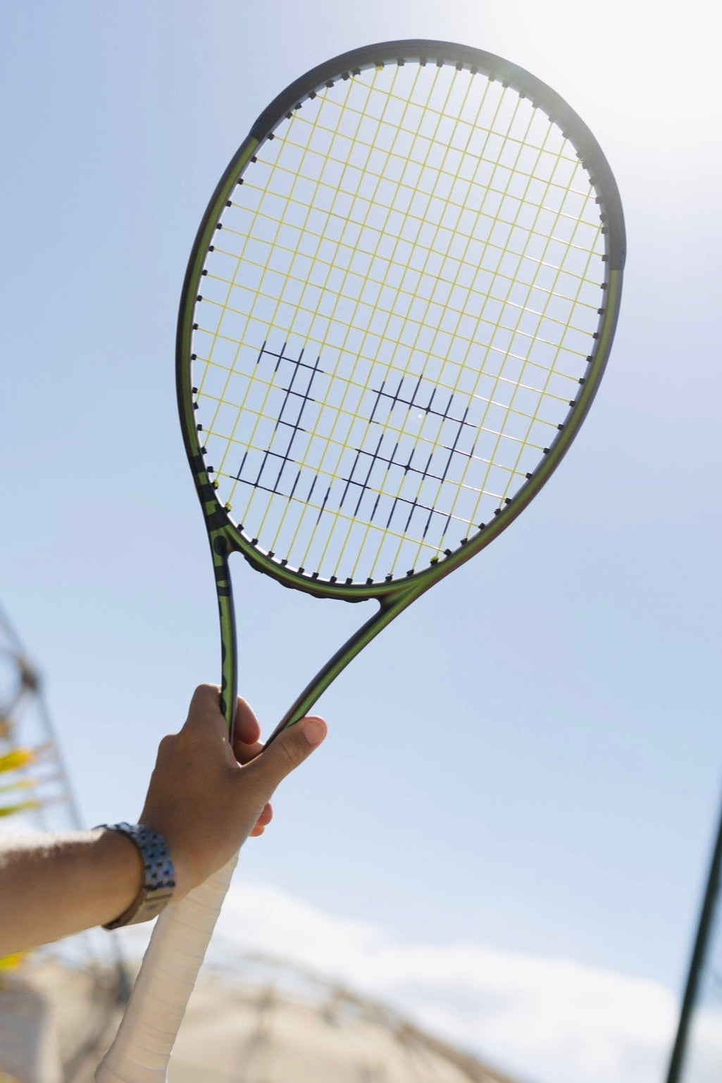 Tennisschläger mit gelben Tennissaiten von BASE12 wird auf dem Platz in die Höhe gehalten“