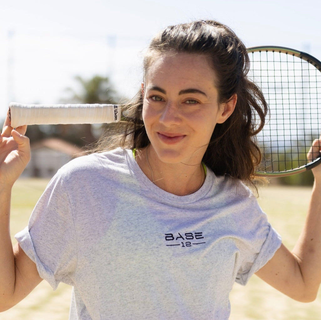 Tennisspielerin trägt ein BASE12 Shirt und hält einen Tennisschläger auf dem Platz
